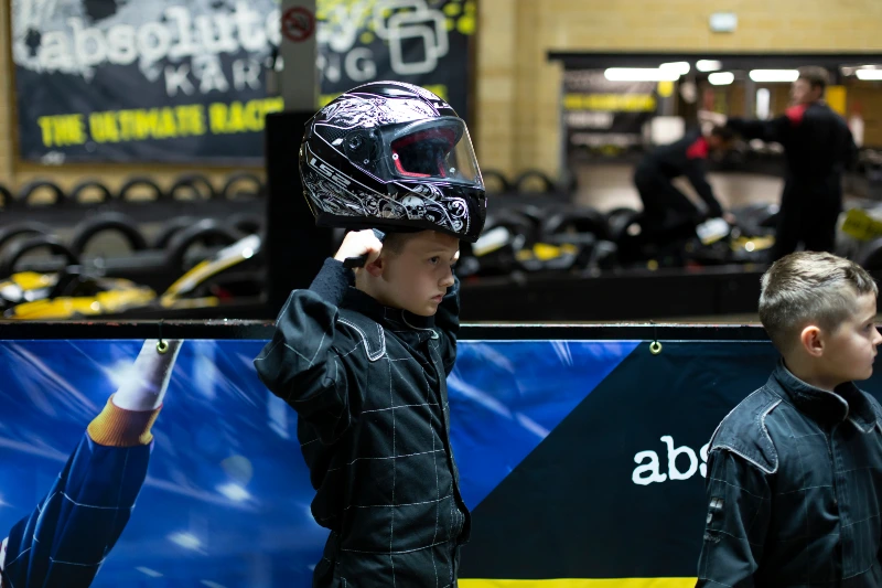 Two children in go karting suits. One is putting a helmet on.