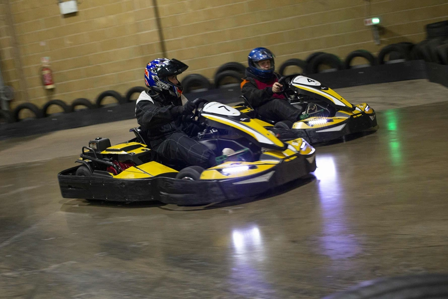 Two people in go karts going round a bend. One is overtaking the other.