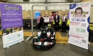 Five people from Wooden Spoon at a karting track, with a person sitting in a twin-seat go kart.
